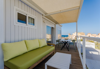 Terraza con sofá verde, mesa y vistas al mar en Bungalow Leo Sea View, Camping Costa del Sol Glamping Village.