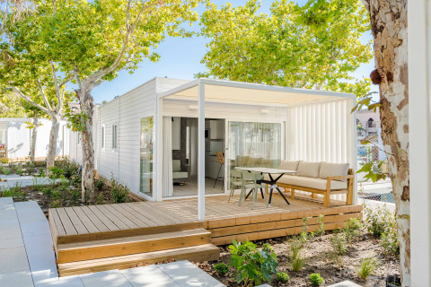Modern lodge with a wooden deck, outdoor seating area, and lush green trees providing shade.