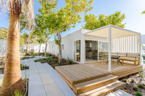 Moderne Lodge mit überdachter Terrasse, Sitzbereich im Freien und grünen Bäumen unter blauem Himmel.