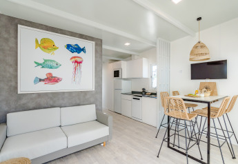 Lyst og moderne lodgeophold med farverig fiskekunst på væggen, køkken, spisebord og fletstole.