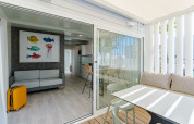 Helles Ferienzimmer mit Sofa, buntem Fischbild, gelbem Koffer und Terrasse mit Sitz- und Essbereich.
