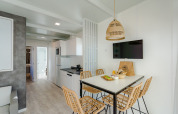 Espacio moderno de lodge con mesa de comedor, sillas de mimbre, cocina, TV de pared y decoración clara.