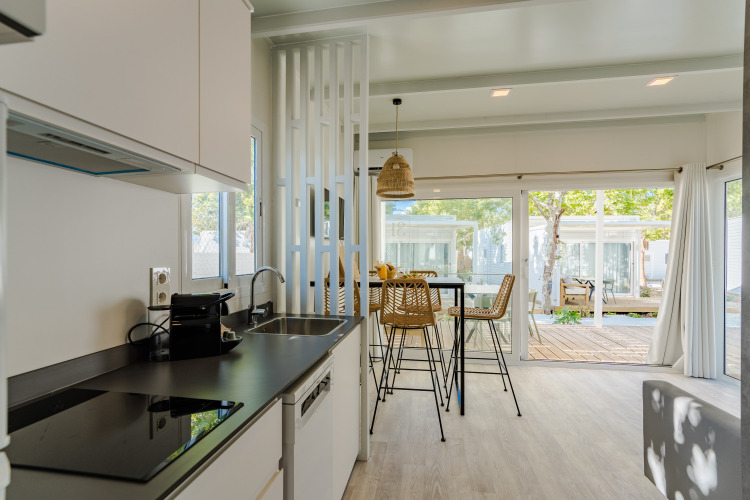 Modern lodge kitchen with dining area, large windows, and view of trees and terrace during daylight.