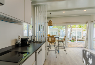 Moderne lodgekøkken med spiseområde, store vinduer og udsigt til træer og terrasse i dagslys.