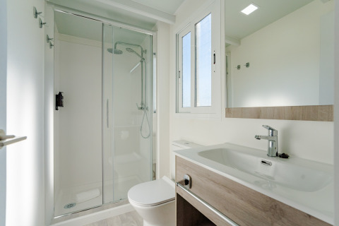 Baño moderno y luminoso en una cabaña con ducha de cristal, lavabo grande, ventana y espejo de pared.