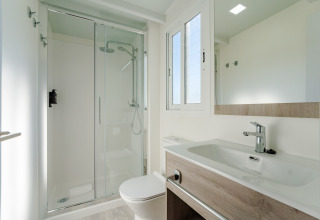 Baño moderno y luminoso en una cabaña con ducha de cristal, lavabo grande, ventana y espejo de pared.