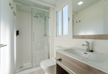 Baño moderno y luminoso en una cabaña con ducha de cristal, lavabo grande, ventana y espejo de pared.