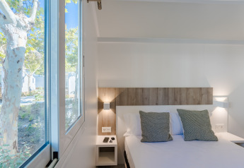 Habitación luminosa en una cabaña con cama doble, cojines verdes y ventana grande con vistas al exterior.