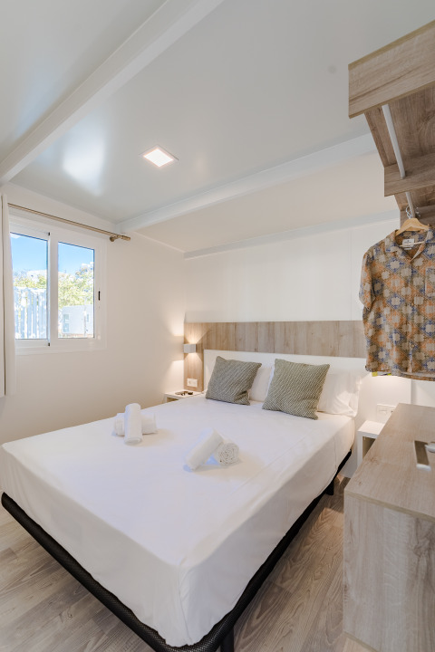 Habitación de cabaña moderna con cama doble, acentos de madera, lámparas y camisa colgada en el perchero.