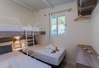 Foto van een moderne lodgekamer met stapelbed, eenpersoonsbedden, speelgoed, raam en houten kast.