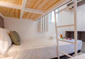 Camera di lodge moderna con letto matrimoniale, biancheria bianca, scala a castello e blocchi colorati sul letto.