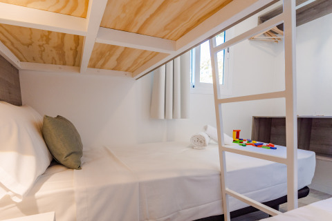 Modern lodge room with double bed, white bedding, bunk ladder, and colorful toy blocks on the bed.