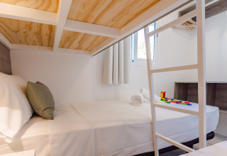 Modern lodge room with double bed, white bedding, bunk ladder, and colorful toy blocks on the bed.