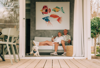 Coppia con cane che beve vino sul divano nel Bungalow Neri Pet Friendly, Costa del Sol Glamping Village, Spagna.