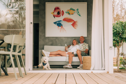 A couple enjoys wine with their dog on a sofa at Bungalow Neri Pet Friendly, Costa del Sol Glamping Village, Spain.