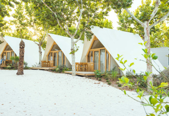 Witte A-frame glampinglodges met houten terrassen tussen bomen bij Camping Costa del Sol Glamping Village, Spanje.
