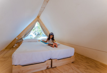 A girl reads a book on a bed inside a cozy A-frame lodge at Camping Costa del Sol Glamping Village, Spain.