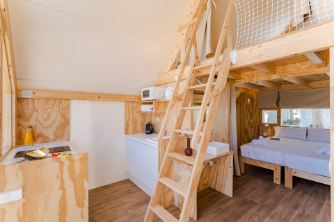 Interior del lodge Hanna, con decoración de madera clara, altillo, cocina y cama doble en Camping Costa del Sol Glamping Village.