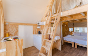 Interior del lodge Hanna, con decoración de madera clara, altillo, cocina y cama doble en Camping Costa del Sol Glamping Village.