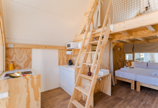Interieur van Hanna-lodge met lichte houten inrichting, slaapzolder, keukenblok en bed bij Camping Costa del Sol Glamping Village.