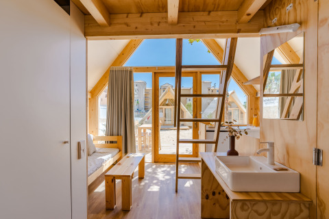 Interior de cabaña de madera con altillo y puerta de cristal en Hanna, Camping Costa del Sol Glamping Village, España.