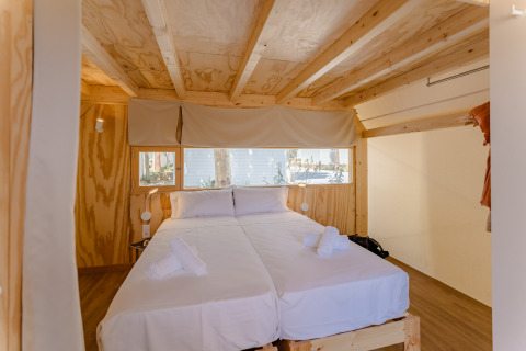 Dormitorio de cabaña de madera con dos camas, sábanas blancas y ventanales en Camping Costa del Sol Glamping Village.