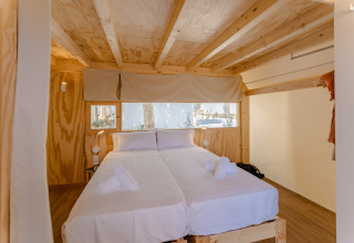 Dormitorio de cabaña de madera con dos camas, sábanas blancas y ventanales en Camping Costa del Sol Glamping Village.