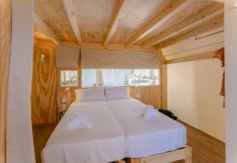 Soveværelse i en træhytte med to senge, hvide lagner og store vinduer på Camping Costa del Sol Glamping Village.