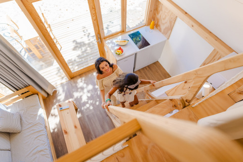 Une mère et sa fille montent un escalier en bois dans un lodge lumineux de Camping Costa del Sol Glamping Village, Espagne.
