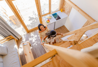 Une mère et sa fille montent un escalier en bois dans un lodge lumineux de Camping Costa del Sol Glamping Village, Espagne.
