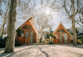 Zwei A-förmige Holzhütten unter kahlen Bäumen im Sonnenlicht im Camping Costa del Sol Glamping Village.