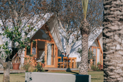 Due persone si rilassano davanti a una baita al Camping Costa del Sol Glamping Village in Spagna, tra gli alberi.