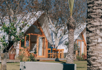 Two people relaxing outside a cozy lodge at Camping Costa del Sol Glamping Village in Spain, surrounded by trees.