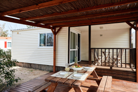 Terraza de madera exterior en el Bungalow Essential Golero con mesa de picnic, puesta para cuatro y frutero.
