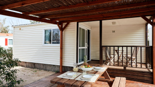 Terraza de madera exterior en el Bungalow Essential Golero con mesa de picnic, puesta para cuatro y frutero.
