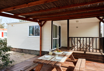 Terrasse extérieure en bois du Bungalow Essential Golero avec table de pique-nique dressée pour quatre et panier de fruits.