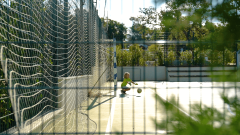 Niño juega con una pelota en una cancha soleada del Camping Lanterna, un parque vacacional en Istria, Croacia.