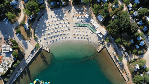 Vista aerea del Camping Lanterna in Istria, Croazia, con spiaggia, ombrelloni bianchi e mare cristallino.