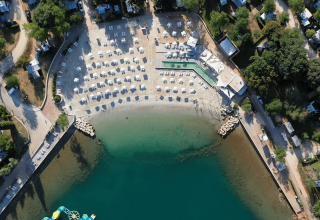 Luftfoto af Camping Lanterna feriepark i Istrien, Kroatien med strand, parasoller og smaragdgrønt vand.