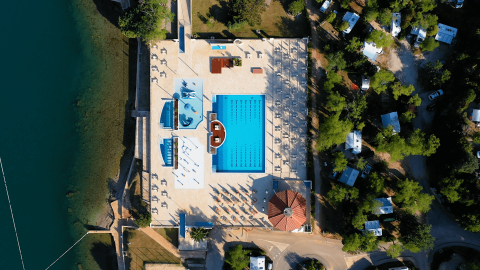 Vista aerea della piscina e area relax al Camping Lanterna in Istria, Croazia, circondata da alberi e camper.