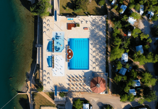 Vista aerea della piscina e area relax al Camping Lanterna in Istria, Croazia, circondata da alberi e camper.