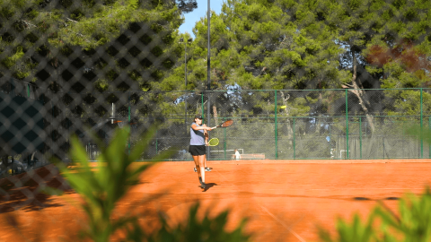 Persona che gioca a tennis su un campo all’aperto circondato da alberi al Camping Lanterna in Istria, Croazia.