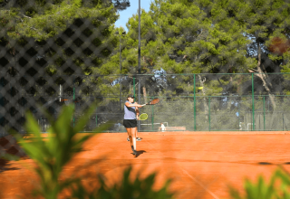 Persona che gioca a tennis su un campo all’aperto circondato da alberi al Camping Lanterna in Istria, Croazia.