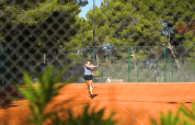 Persona che gioca a tennis su un campo all’aperto circondato da alberi al Camping Lanterna in Istria, Croazia.