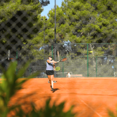 Persona jugando al tenis en una pista exterior rodeada de árboles en Camping Lanterna, Istria, Croacia.