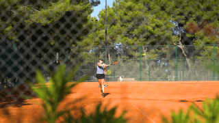 Persona jugando al tenis en una pista exterior rodeada de árboles en Camping Lanterna, Istria, Croacia.