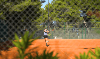 Persona jugando al tenis en una pista exterior rodeada de árboles en Camping Lanterna, Istria, Croacia.