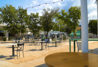 Outdoor dining area with tables and chairs under trees at Camping Lanterna holiday park in Istria, Croatia.