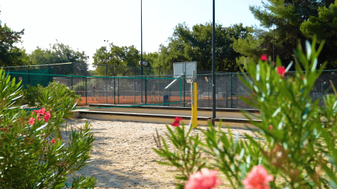 Cancha deportiva de arena con flores en primer plano y pistas de tenis detrás, Camping Lanterna, Istria, Croacia.