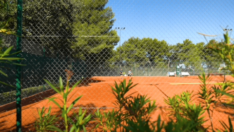 Vista de una pista de tenis de arcilla en Camping Lanterna, rodeada de vegetación, en Istria, Croacia.
